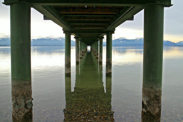underneath view of pier on a lake with mountains in background