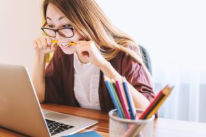 woman looking at screen biting pencil